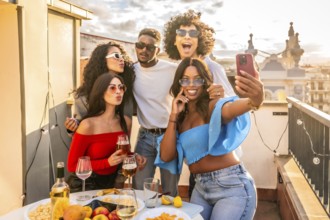 Happy multi-ethnic friends taking selfie celebrating evening party in rooftop drinking wine and