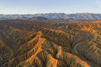 River bed runs through a landscape of eroded hills, badlands at sunset, mountain peaks of the Tian