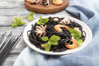 Black cuttlefish ink pasta with shrimps or prawns and small octopuses on gray wooden background and