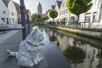 Bronze sculpture by Cornelia Brader: City tomcat Chicco at the city stream, behind it Our Lady's