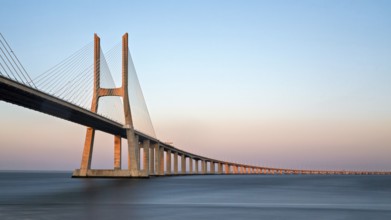 A long cable-stayed bridge spans over water under a gradient sunset sky, Lissabon, Vasco Da