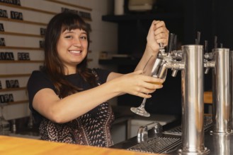 A cheerful waitress serves a glass of beer from a tap in a modern bar. She smiles and enjoys her