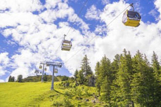 Several cable cars travelling across a green meadow under a cloudy sky, Penken, Zillertal, Austria,