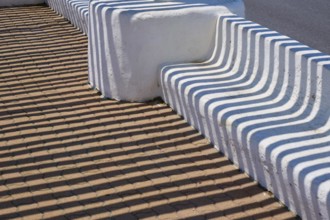 White concrete bench with geometric shadow patterns on a brown floor, Saintes-Maries-de-la-Mer,