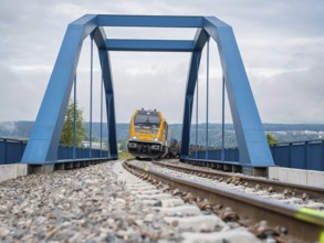 Yellow train on blue bridge over rails on a cloudy day, track construction, rail delivery for