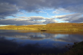 A calm lake reflects the cloudy sky and the surrounding landscape, October, Hebrides, Isle of Skye,