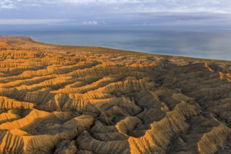 Landscape of eroded hills, badlands at sunset, Lake Issyk Kul in the background, aerial view,