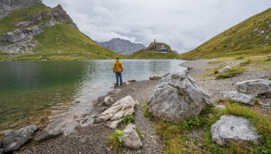 Mountaineer in yellow jacket at the mountain lake, view over the Wolayersee lake to the alpine club