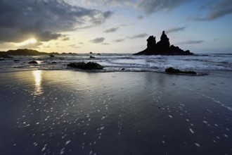 Dramatic cloudy atmosphere with rock formation at rising tide at sunset on the beach of Playa de