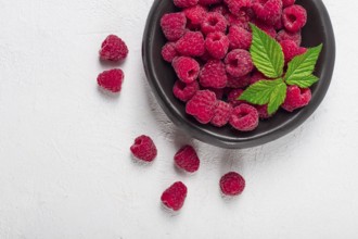 Fresh raspberries, on a black plate, with leaves, top view, on a white table