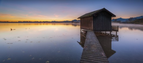 Boathouse on Lake Chiemsee at sunrise, fog rising, the Chiemgau Alps in the background, Chiemgau,