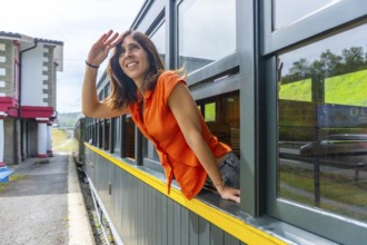 A woman in an orange shirt is looking out the window of a train. The train is yellow and green