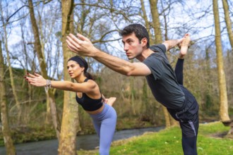Yoga teachers performing a balancing asana by a river in the forest, enjoying the benefits of