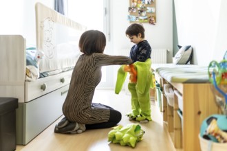 Mother assisting her son in getting dressed in a dinosaur costume, fostering imaginative play in a
