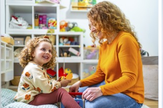 Caucasian adult mother and girl playing with toys sitting in the bedroom at home