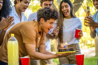 Happy young man with with birthday cake celebrating with friends at park