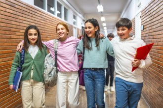 Four cheerful students are walking together in school corridor, carrying backpacks and notebooks