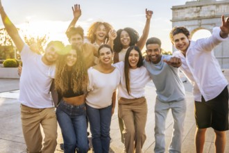 Portrait of diverse group of cheerful young people having fun and raising arms while standing