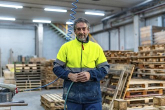 Portrait of a mature man manual worker with reflective clothes in a recycling plant full of pallets