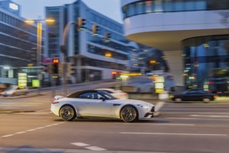 Car at night in front of urban surroundings with modern architecture, pull-along. Mercedes-Benz SL