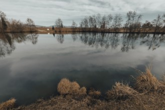 Tranquil pond with reflection of trees and clouds, surrounded by a natural landscape, Drudenteich,