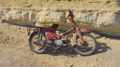 An old Honda C50 motorbike stands abandoned in front of a rocky cliff, Paralia Agios Theodoros