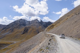 Car on narrow gravel track in mountain landscape at Chong Ashuu Pass, Tian Shan Mountains,