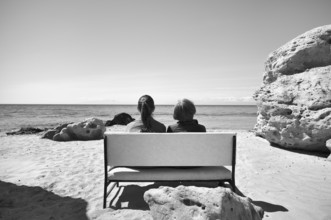 Two woman sitting on a bench, rocks on the beach of Nea Kallikratia, Chalkidiki, Halkidiki,