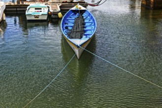 A blue fishing boat with a net lies quietly in a sunny harbour, small town of Vila Franca do Campo,