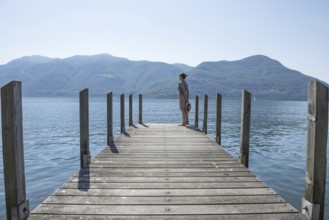 Woman Standing on a Pier on Lake Maggiore with Mountain in a Sunny Day in Brissago, Ticino,