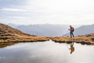 Mountaineer hiking with poles, reflected in a small mountain lake on the Krahberg, mountain