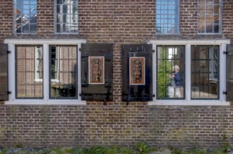 Facade of a brick building with mullioned windows and dark shutters, reflections in the glass,