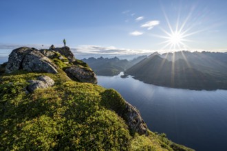 Mountaineer on the summit of Dronningsvarden or Stortinden, behind sea and fjord Umvågsundet,