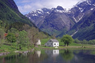 A white house on a calm lake, surrounded by green trees and majestic snow-capped mountains under a