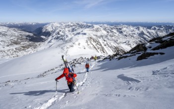 Ski tourer on foot, carrying skis on backpack, mountain panorama, snow-covered mountain landscape