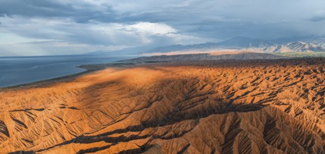Landscape of eroded hills, badlands at sunset, Issyk Kul Lake in the background, aerial view,