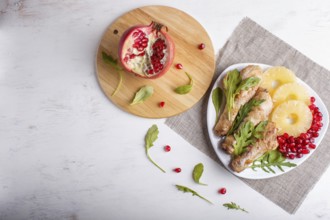 Fried chicken legs with rucola, pineapple and pomegranate seeds on white wooden background, copy