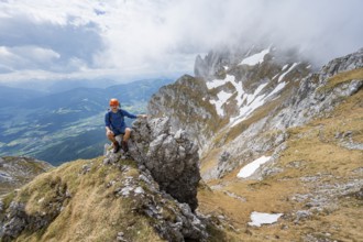 Mountaineer with helmet sitting on a rock, ascent to the Maukspitze, clouds moving around the