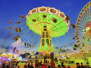 The colourfully illuminated Wellenflug chain carousel and the Ferris wheel in the evening, Cranger