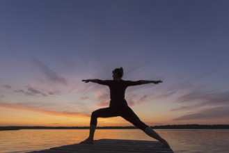 Woman practicing yoga posture Virabhadrasana II, Warrior Pose, lunging standing asana on jetty at