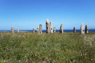 Group of standing stones in a meadow, surrounded by nature and under a blue sky with the sea in the