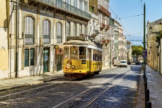 A historic yellow tram travels down a sunny Lisbon street lined with old buildings under a clear