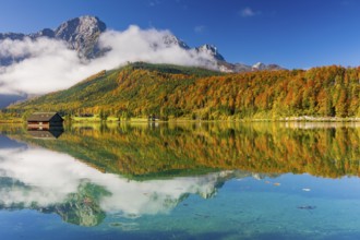 Lake Almsee in autumn with a forest reflected in the lake. A slowly dissipating fog moves over the