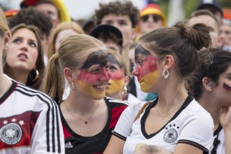Women wearing make-up in the German national colours watch the football match in the fan zone at