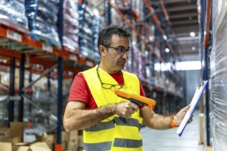 Mature caucasian man taking inventory using barcode reader and clipboard in a storage warehouse