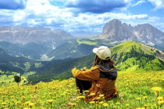 Woman hiker sitting in a vibrant flower field, admiring the stunning seceda peaks rising