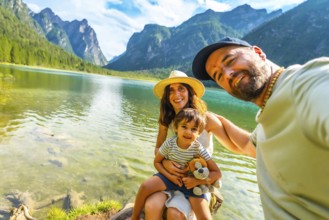 Happy family taking a selfie by the transparent water of lake dobbiaco with the dolomites in the