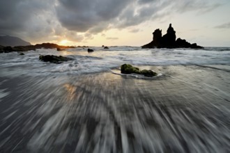 Dramatic cloudy atmosphere with rock formation at rising tide at sunset on the beach of Playa de