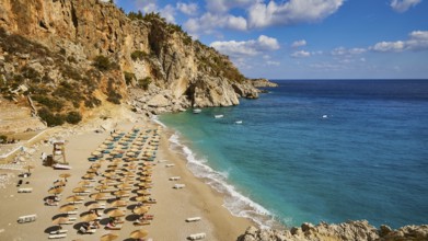 A wide view of a coastline with a beach lined with parasols and turquoise blue water, Kyra Panagia,
