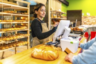 Friendly young latin saleswoman preparing the checkout for a client in an artisan bakery